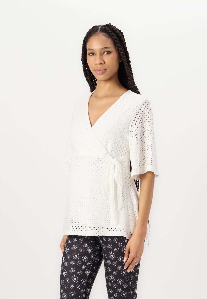Witte, korte mouwen wikkeltop van broderie met een strikdetail in de taille, gecombineerd met zwarte bloemenprint broek.