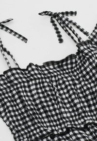 Schwarz-weißer karierter Kleid mit dünnen Schulterträgern, rüschierten Kanten und elastischem Taillenbund, der ein Gingham-Muster aufweist.