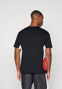 Camiseta de algodón negra de manga corta, con paneles laterales en blanco y rojo. Textura suave con cuello redondo y ajuste relajado.