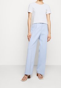 T-shirt corto grigio chiaro abbinato a pantaloni larghi azzurri a vita alta. Sandali bianchi con cinturini e tacco spesso. Tessuto dalla texture liscia.
