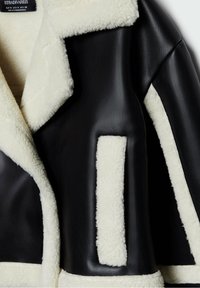 Chaqueta de cuero negra con borde de borrego blanco, que presenta un cuello con muesca, un bolsillo de parche y rayas contrastantes a lo largo de los lados.