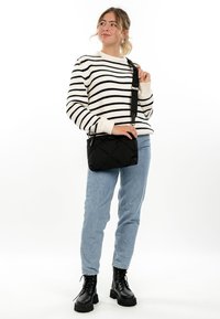 Young woman in striped sweater, light blue jeans, black boots, carrying a black crossbody bag, gazing slightly to the side.