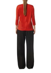 Rotes Langarmoberteil aus einem weichen Material, kombiniert mit lockeren schwarzen Hosen, die eine glatte Textur und einen geraden Schnitt aufweisen.