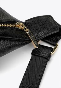 Borsa nera in pelle con superficie texture, zip e accenti metallici dorati, dotata di una tracolla intrecciata nera e un'etichetta rettangolare.