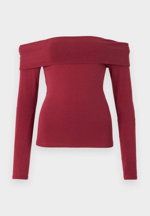 Viininpunainen, hihaton pitkähiha. Tiukka muotoilu, sileä pinta ja leveä kaula-aukko. Yksinkertaiset, minimalistiset tikkaukset hihansuissa ja helmassa.