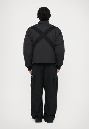 Černá péřová bunda s výrazně zkráceným designem, s detaily křížového popruhu na zadní části. V kombinaci s širokými černými cargo kalhotami.