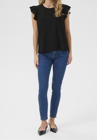 Blusa nera a maniche corte con spalle arricciate e dettagli in pizzo, abbinata a jeans blu slim-fit e ballerine nere a punta.