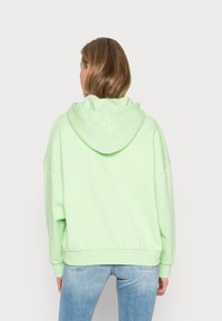 Felpa oversize verde menta con cappuccio regolabile, orlo a coste e spalle cadute, realizzata in morbido cotone.