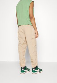 Grön ärmlös topp, beiga cargobyxor med texturerad tyg, och svarta och gröna sneakers med silveraccenter. Avslappnad gatu-mode stil.