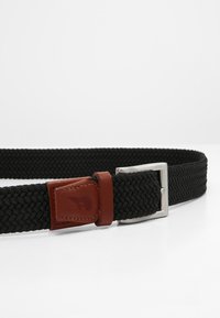 Zwarte gevlochten riem met een zilveren metalen gesp, voorzien van een bruine leren accent nabij de gesp en een textuurpatroon over de hele riem.