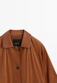 Bruine leren jas met een klassieke kraag, enkele knoopsluiting en een zachte textuur; heeft een zwart label aan de binnenkant.