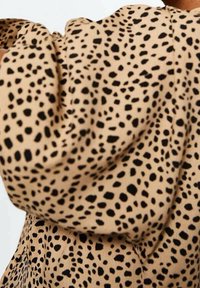 Tela beige con manchas negras irregulares que forman un patrón de estampado de leopardo en una prenda de manga abullonada.