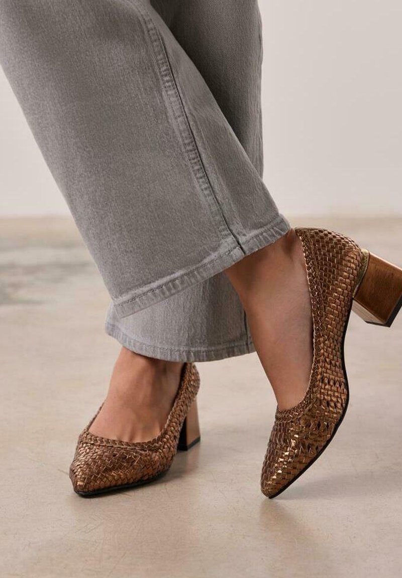 Chaussures à talons hauts tissées marron avec un bout carré et un talon bloc, complétées par un pantalon cropped gris clair dans un cadre neutre.