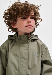 Wodoodporna kurtka w oliwkowej zieleni z kapturem, z zapięciami na guziki i logo na piersi. Gładka faktura, lekki materiał.