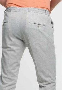 Man som har på sig ljusgrå byxor och en orange skjorta, sedd från midjan och neråt bakifrån.