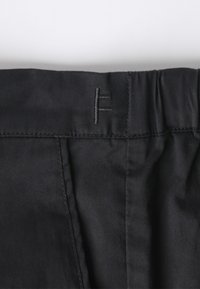 Black fabric waistband with stitched detailing and a small embroidered logo. Material has a smooth texture and appears durable.