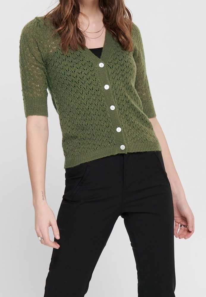 Oliwkowy sweter dzianinowy z dekoltem w szpic, krótkimi rękawami i zapięciem na guziki. Posiada wzór w romby i prążkowany dół. Połączony z czarnymi spodniami.