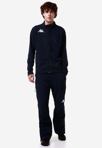 Giacca e pantaloni in pile di colore blu navy. La giacca presenta una chiusura con zip e un logo. I pantaloni hanno tasche laterali e una vestibilità ampia.