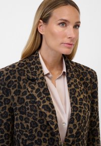 Leopardenmuster Blazer aus braunem und schwarzem Stoff, mit einem Reverskragen, einem Einzelknopfverschluss und einem kontrastierenden hellrosa Hemd darunter.