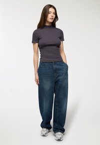 Czarnoszary, dopasowany top z krótkim rękawem, zestawiony z luźnymi, niebieskimi dżinsami, które mają boczne kieszenie i lekko wyblakłą fakturę.
