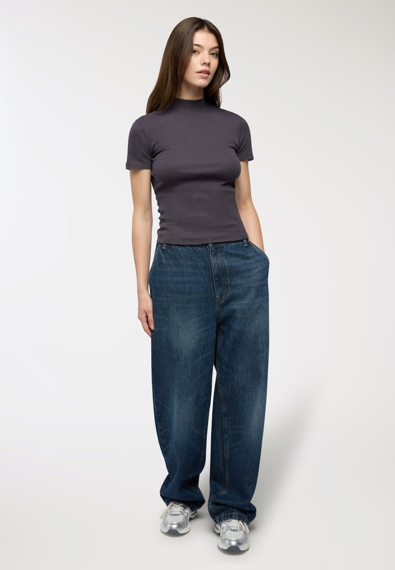 Czarnoszary, dopasowany top z krótkim rękawem, zestawiony z luźnymi, niebieskimi dżinsami, które mają boczne kieszenie i lekko wyblakłą fakturę.