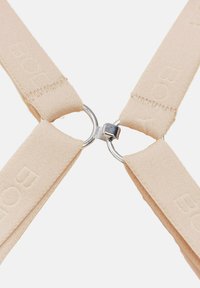 Cinghie in suede beige collegate da due anelli di metallo argentati intrecciati con una piccola chiusura al centro su uno sfondo bianco.