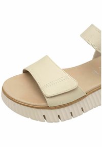 Beige open-toe sandal with wide leather straps, cushioned footbed, and thick ridged rubber sole for added comfort and grip.