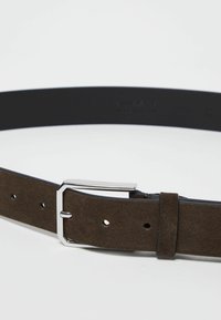 Cintura in suede marrone con retro in pelle nera, dotata di una fibbia rettangolare in argento e cinque fori regolabili. Texture complessivamente liscia.