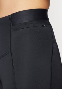Fekete sport leggings sima, elasztikus derékpánttal és textúrázott varrással rendelkeznek az összes varrás mentén, valamint egy kis zsebbel.