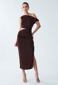 Vestito marrone aderente con design asimmetrico sulla spalla, vita con ritagli e dettagli arricciati, caratterizzato da una spacco laterale e tessuto dalla texture liscia.