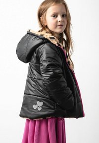 Czarna kurtka puchowa z kapturem wyłożonym futrem, różowym zamkiem błyskawicznym i grafiką serc po bokach. Nosi się ją na różowej spódnicy plisowanej.