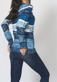 Blå stickad tröja med olika nyanser, med ett texturerat mönster och långa ärmar, kombinerad med mörka jeans.