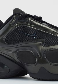 Juodas sportinis batelis su struktūruota akių viršuje, blizgiomis detalėmis ir paminkštintu padu. Ypatybėse yra ryškus Nike logotipas ir sklandžios dizaino detalės.