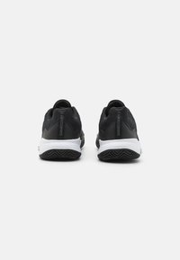 Baskets de sport noires avec une tige texturée, une semelle intercalaire blanche et une semelle extérieure noire à motifs. Présente le logo "GAMECOURT 2" sur le talon.