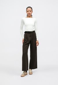 Long-sleeve white top with a square neckline, paired with high-waisted dark brown wide-leg trousers and tan patterned sneakers.