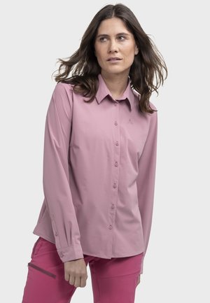 Langärmliges Hemd in weichem rosa Stoff, mit Kragen, dezentem Logo und Knopfmanschetten. Kombiniert mit einer rosa Hose.