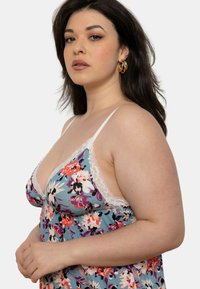 Nuisette fleurie avec un fond bleu clair, bordure en dentelle blanche au niveau du col et des bretelles, ornée de motifs vifs en rose, violet et noir.