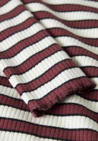 Soonikkoeline kangas, mille on horisontaalsed triibud burgundia ja valge värviga ning peenikesed mustad aktsendid. Tekstuur on pehme, kergelt kuluva äärega.