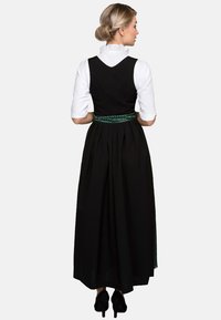 Schwarzes traditionelles Kleid mit tailliertem Oberteil, weißer Bluse, grünen Bandakzenten und gefälteltem Rock, in einem bodenlangen Design.