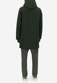 Svart huvmantel med rak skärning, som har en slät textur och minimalistisk design. I kombination med grå byxor och vita sneakers.