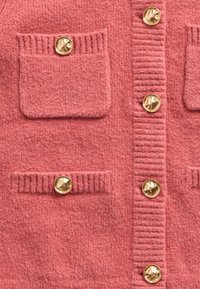 Texturált rózsaszín kardigán két mellzsebbel. Arany gombokkal és bordázott részletekkel a zsebek mentén és a középső részen. Puha anyagból készült.