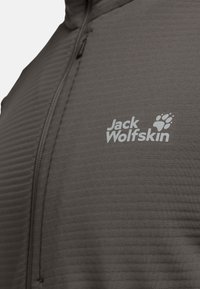Veste gris zippée avec une texture côtelée et un petit logo blanc "Jack Wolfskin" sur la poitrine, mettant en avant un design sportif.