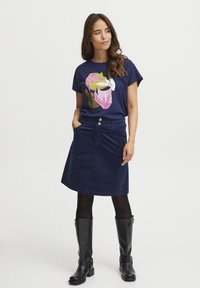 T-shirt di cotone blu navy con stampa floreale colorata; abbinato a una gonna di velluto a coste blu navy lunghezza ginocchio, stivali neri al ginocchio.