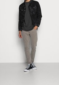 Czarna kurtka dżinsowa z kieszeniami na piersi, szara koszulka pod spodem, jasnoszare spodnie slim-fit i czarne trampki za kostkę z białymi podeszwami.