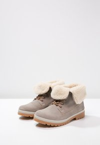 Jasnoszare zamszowe buty z miękkim kremowym futerkiem z sztucznego futra przy mankiecie, brązowymi sznurowadłami i trwałą, teksturowaną podeszwą. Odpowiednie na chłodniejszą pogodę.