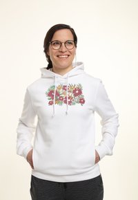 Sudadera blanca con capucha que presenta un colorido diseño floral en el pecho, con cordones y un bolsillo frontal. Tejido de textura suave.