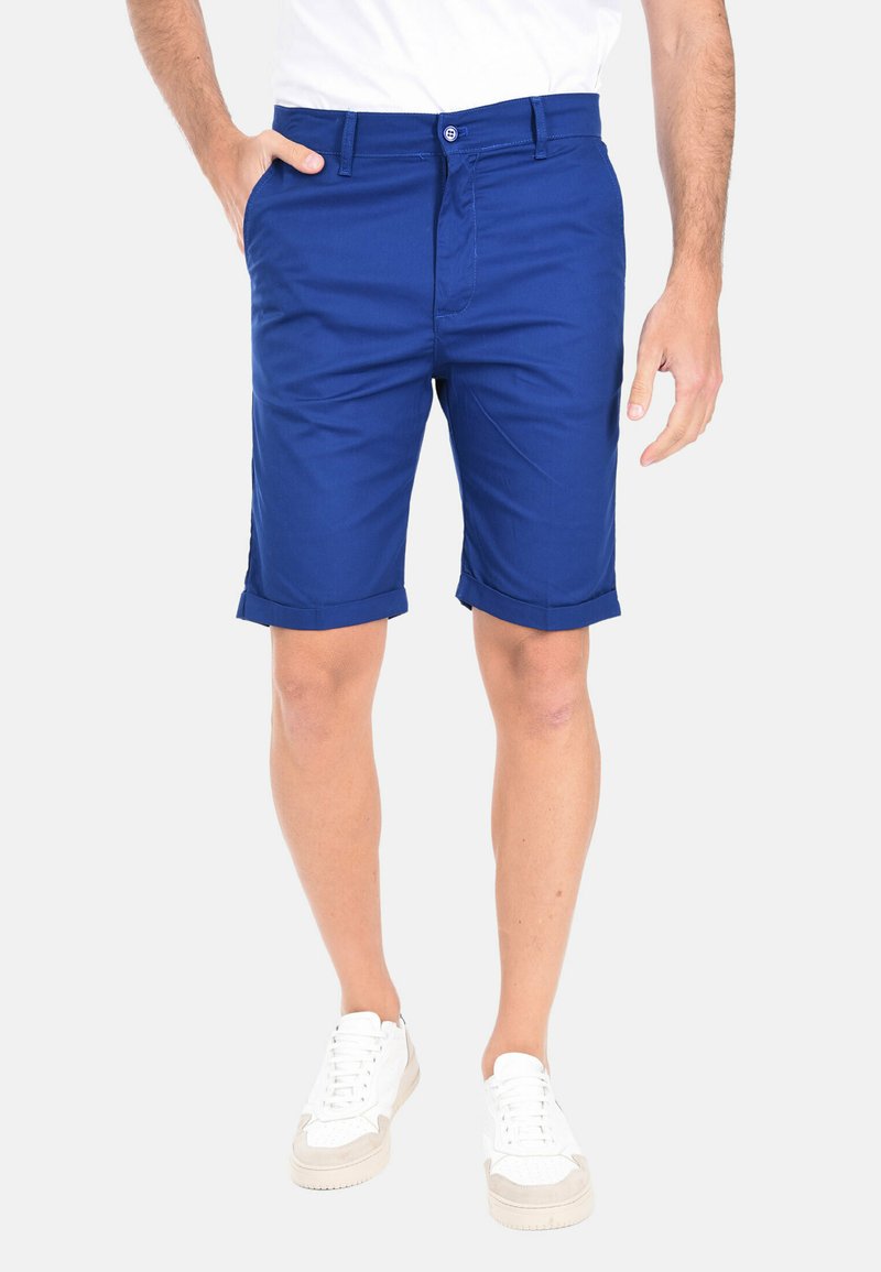Pantaloni shorts blu al ginocchio realizzati in tessuto leggero, con chiusura frontale a bottoni e orli arrotolati. Abbinati a sneakers bianche.