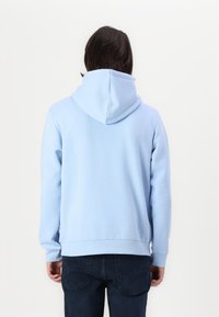 Lys blå hettegenser med en myk tekstur, lange ermer og ribbestrikkede mansjetter og kant. Har et minimalistisk design og kengurulomme.