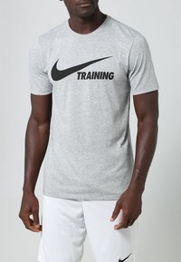 Camiseta deportiva de manga corta gris con el texto "TRAINING" en negro y el logo de Nike. Fabricada con material suave y transpirable. Diseño simple.