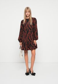 Black dress with red swirling pattern, long puff sleeves, and ruffled hem, paired with black bow-heeled shoes and a small white handbag.